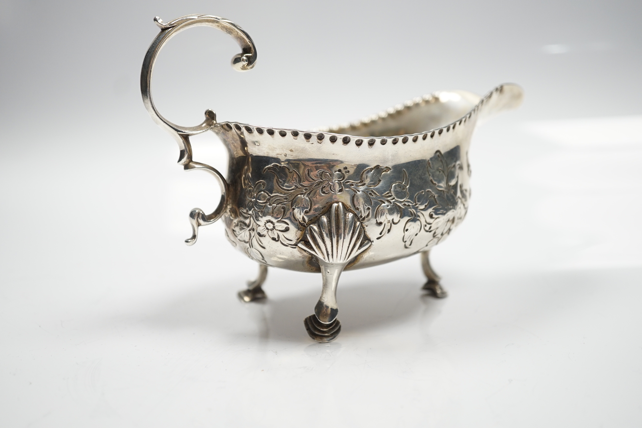 A George III silver sauce boat, with flying scroll handled and later embossed decoration, maker T?, London, 1776, length 15.5cm, 5.75oz.